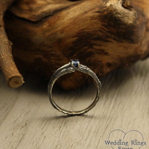 May include: A silver ring with a dark blue gemstone set in a branch-like design. The ring is on a wooden surface.