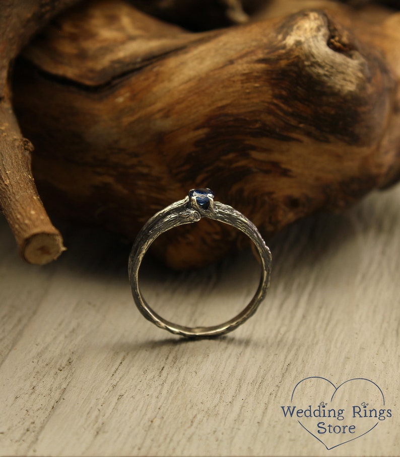 May include: A silver ring with a dark blue gemstone set in a branch-like design. The ring is on a wooden surface.