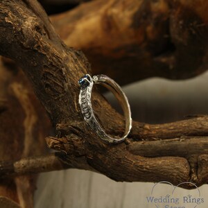 May include: A silver wedding band with a blue gemstone set in the center. The band has a textured, organic design.