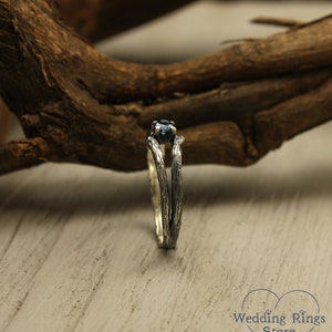 May include: A silver ring with a blue gemstone set in a branch-like design. The ring is on a wooden surface.
