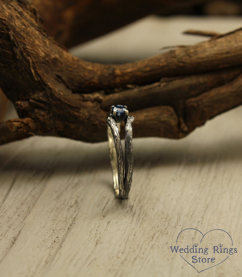 May include: A silver ring with a blue gemstone set in a branch-like design. The ring is on a wooden surface.