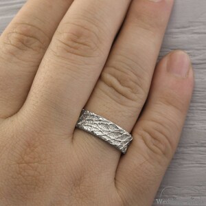 May include: A silver ring with a textured, organic design. The ring is worn on a person's finger.