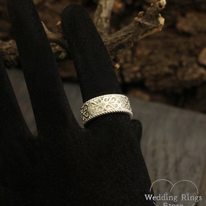 May include: A silver filigree wedding band with a twisted rope design. The band is on a black velvet ring display.