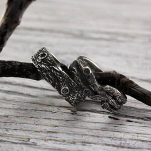 May include: Two silver rings with a tree bark design. The rings are intertwined and have a rustic look.