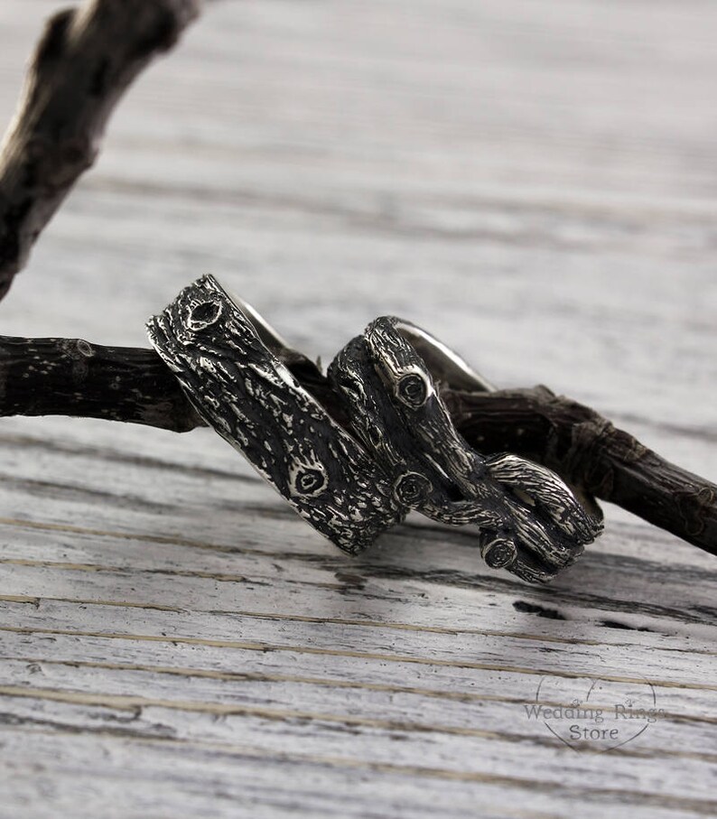 May include: Two silver rings with a tree bark design. The rings are intertwined and have a rustic look.