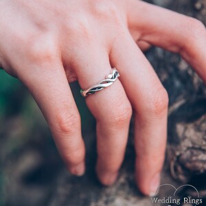 May include: A silver wedding band with a braided design. The band is worn on a finger.