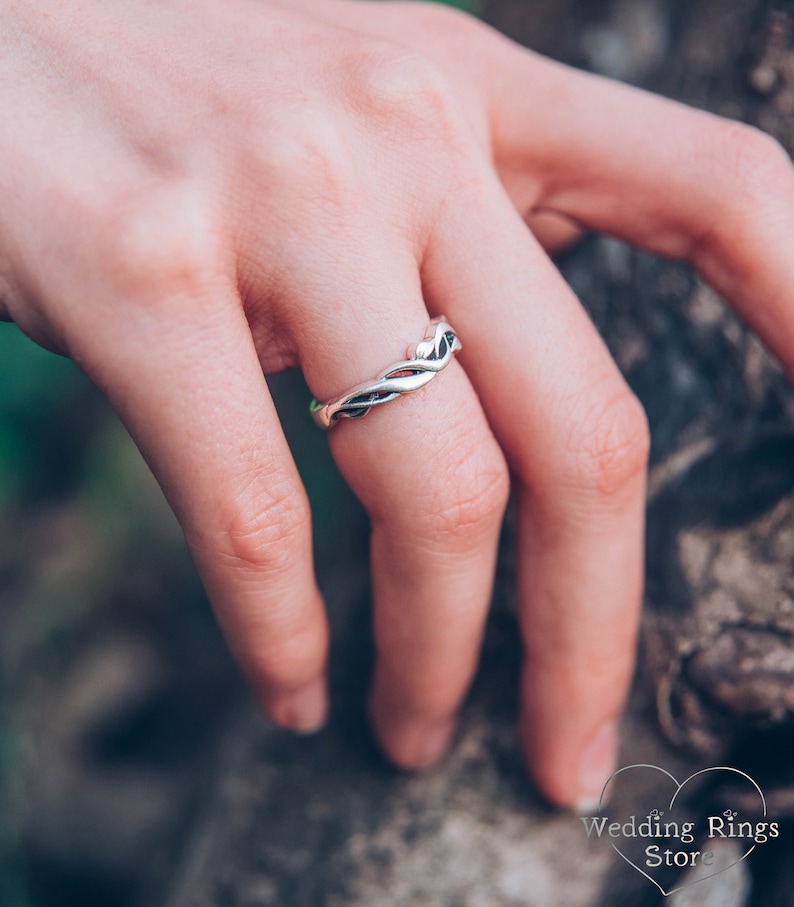 May include: A silver wedding band with a braided design. The band is worn on a finger.