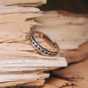 Op de afbeelding: Een zilveren trouwring met een patroon van zwarte diamanten. De ring ligt op een stuk hout.