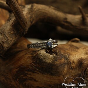 May include: A silver ring with a blue gemstone and small diamonds set in a textured band. The ring is on a piece of wood.