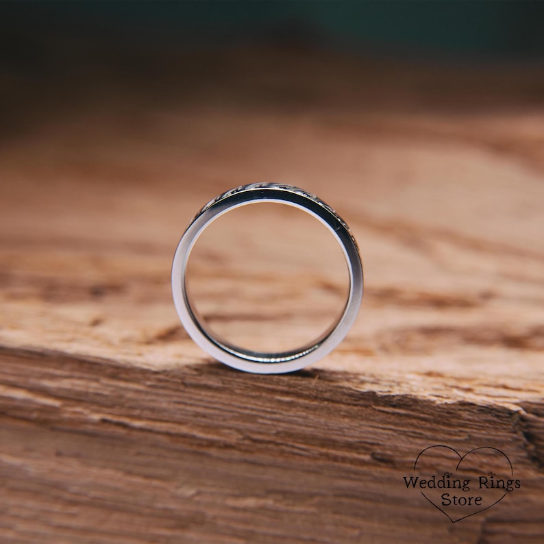 Op de afbeelding: Een zilveren trouwring met een getextureerd ontwerp. De ring ligt op een houten oppervlak.