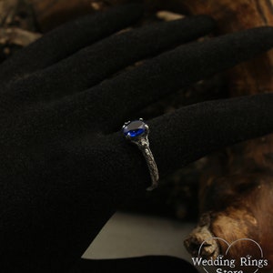 May include: A silver ring with a blue gemstone set in a claw setting. The ring band is textured and has a branch-like design.