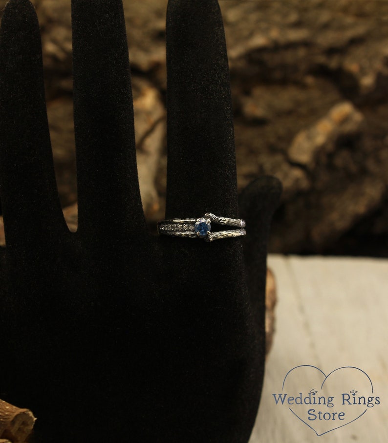 May include: A silver ring with a blue gemstone and a delicate, twisted band. The ring is set on a black velvet background.