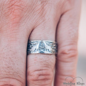May include: A silver wedding band featuring a design of two wolves howling at the moon. The band is textured and has a rustic look.