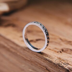 Op de afbeelding: Een zilveren trouwring met een zwart patroon. De ring ligt op een houten oppervlak.