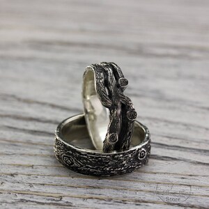 May include: Two silver rings with a textured wood-like design. The top ring features a twisted branch design with small black gemstones. The bottom ring has a more subtle wood grain pattern.