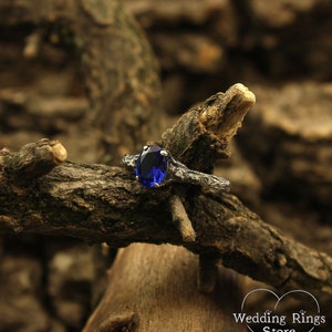 May include: A silver ring with a dark blue oval gemstone set in a branch-like design. The ring is resting on a piece of weathered wood.