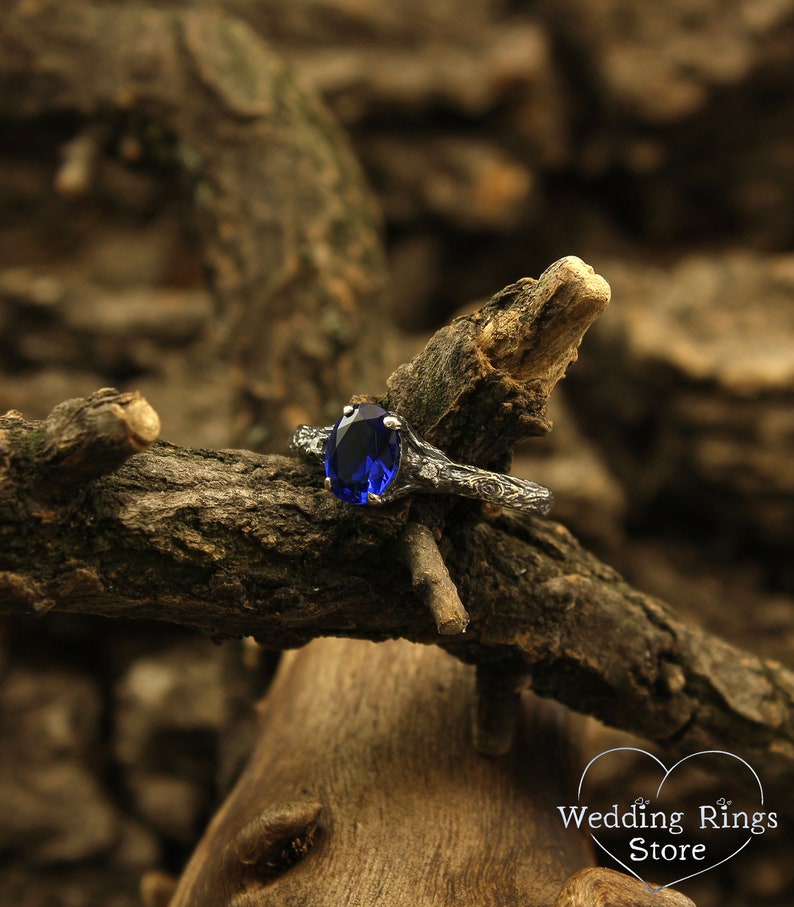 May include: A silver ring with a dark blue oval gemstone set in a branch-like design. The ring is resting on a piece of weathered wood.