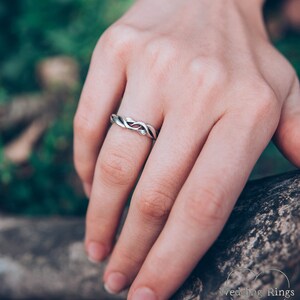 May include: A silver wedding band with a twisted design. The band is worn on a person's finger.
