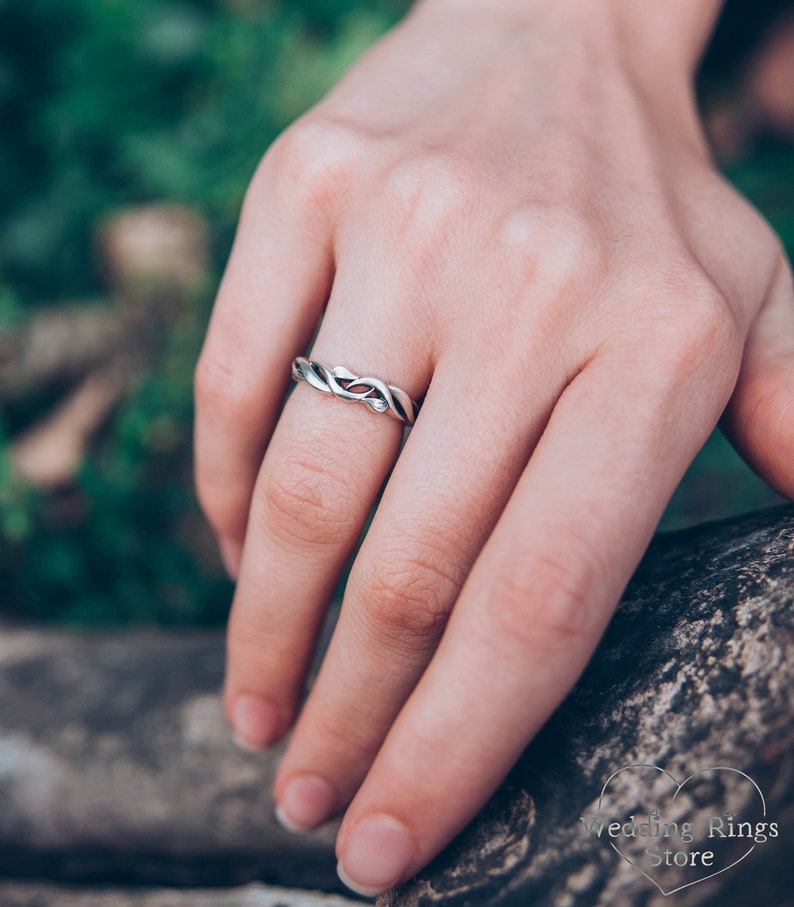 May include: A silver wedding band with a twisted design. The band is worn on a person's finger.