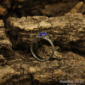 May include: A silver ring with a blue gemstone set in a branch-like design. The ring is on a rough, brown, textured surface.