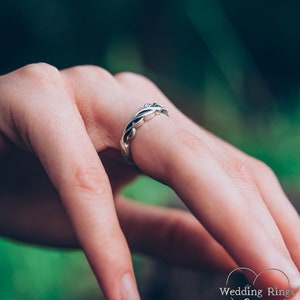 May include: A silver wedding band with a braided design. The band is worn on a finger.