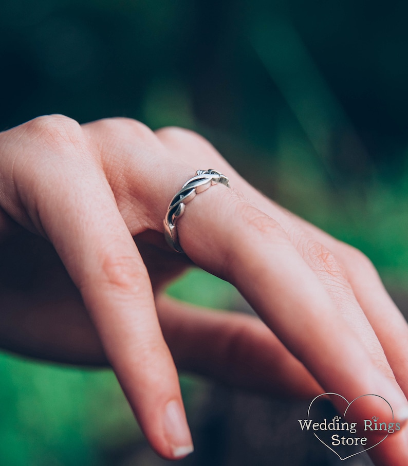 May include: A silver wedding band with a braided design. The band is worn on a finger.