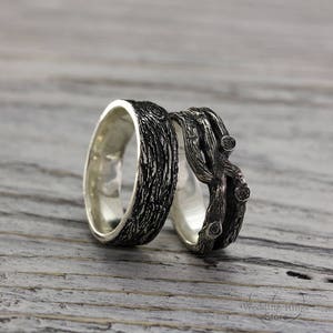 May include: A pair of silver wedding bands with a unique design. One band features a textured wood-like pattern, while the other band is shaped like intertwined branches.