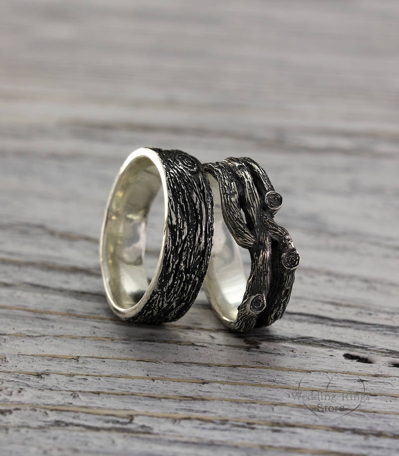 May include: A pair of silver wedding bands with a unique design. One band features a textured wood-like pattern, while the other band is shaped like intertwined branches.