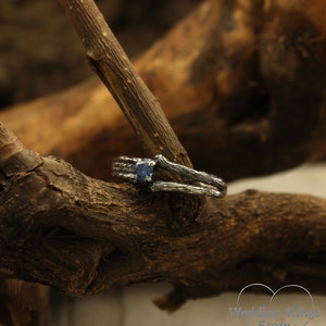 May include: A silver ring with a blue gemstone set in a branch-like design. The ring is resting on a piece of weathered wood.