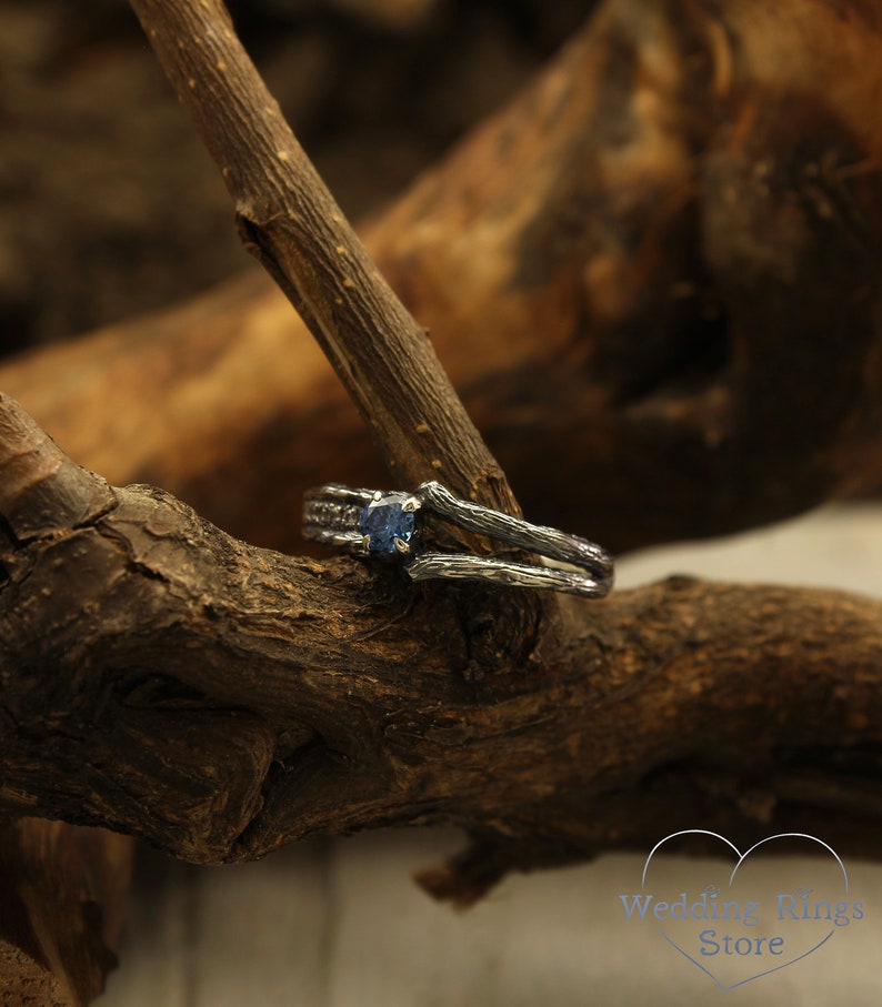 May include: A silver ring with a blue gemstone set in a branch-like design. The ring is resting on a piece of weathered wood.