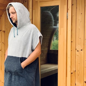 May include: A person wearing a grey and black hooded towel robe with a blue drawstring. The person is standing in front of a wooden door.