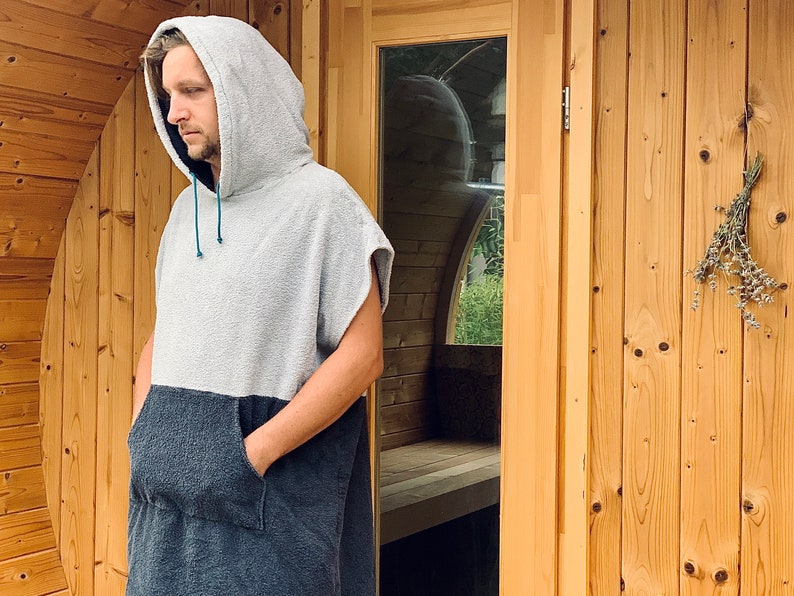 May include: A person wearing a grey and black hooded towel robe with a blue drawstring. The person is standing in front of a wooden door.