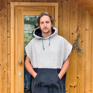 May include: A person wearing a grey and black hooded poncho with a blue drawstring. The poncho has a large pocket on the front.