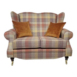 May include: A two-seater sofa with a plaid upholstery in shades of beige, red, and yellow. The sofa has a wingback design and features two orange velvet cushions.