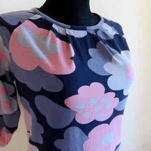 May include: A navy blue, long-sleeved shirt with a floral print featuring pink and gray flowers. The flowers are stylized and resemble clouds.