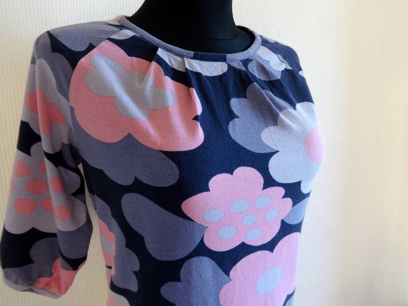 May include: A navy blue, long-sleeved shirt with a floral print featuring pink and gray flowers. The flowers are stylized and resemble clouds.