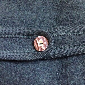 Puede incluir: Primer plano de una tela de punto verde oscuro con un bot&oacute;n marr&oacute;n. El bot&oacute;n tiene un dise&ntilde;o &uacute;nico y est&aacute; cosido a la tela.