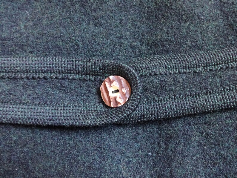 Puede incluir: Primer plano de una tela de punto verde oscuro con un bot&oacute;n marr&oacute;n. El bot&oacute;n tiene un dise&ntilde;o &uacute;nico y est&aacute; cosido a la tela.