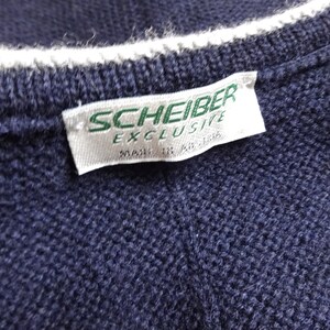 Puede incluir: Una etiqueta blanca con texto verde que dice "Scheiber Exclusive" en un su&eacute;ter de punto azul marino.
