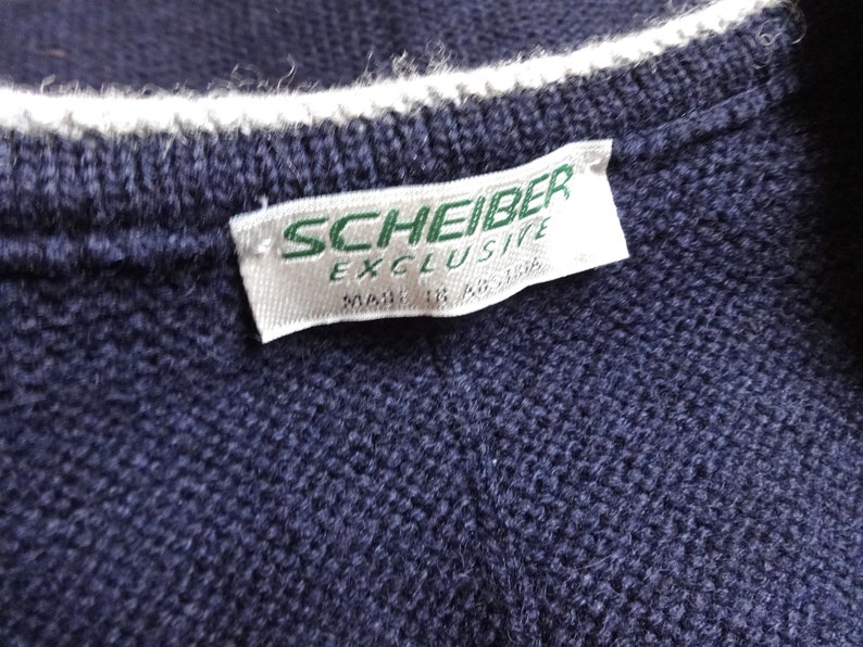 Puede incluir: Una etiqueta blanca con texto verde que dice "Scheiber Exclusive" en un su&eacute;ter de punto azul marino.