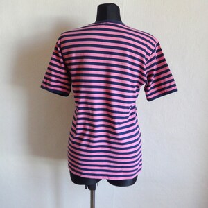 K&ouml;nnte beinhalten: Ein pinkfarbenes und marineblaues gestreiftes T-Shirt mit kurzen &Auml;rmeln.