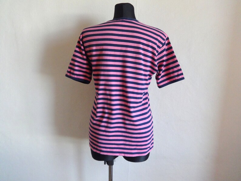 K&ouml;nnte beinhalten: Ein pinkfarbenes und marineblaues gestreiftes T-Shirt mit kurzen &Auml;rmeln.