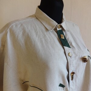 Pu&ograve; includere: Camicia beige con bottoni, dettagli verdi e bottoni decorativi in legno. La camicia ha un colletto classico e una vestibilit&agrave; su misura. Il design include dettagli in tessuto verde e chiusure con bottoni uniche, offrendo un'estetica rustica.