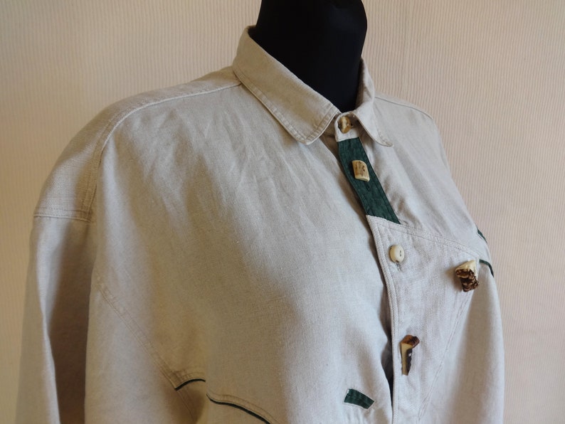 Pu&ograve; includere: Camicia beige con bottoni, dettagli verdi e bottoni decorativi in legno. La camicia ha un colletto classico e una vestibilit&agrave; su misura. Il design include dettagli in tessuto verde e chiusure con bottoni uniche, offrendo un'estetica rustica.