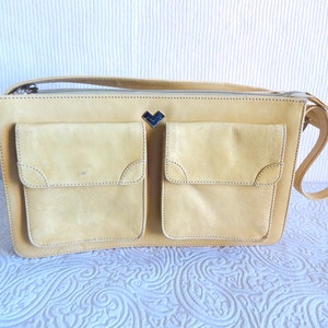 May include: A light yellow leather shoulder bag with two large front pockets and a small metal heart-shaped logo.