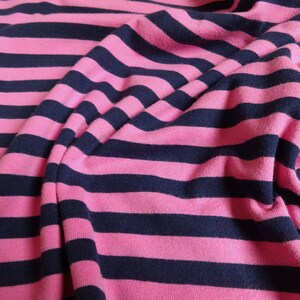 K&ouml;nnte beinhalten: Rosa-blauer gestreifter Stoff mit weicher, strukturierter Haptik. Der Stoff ist gefaltet und drapiert, wodurch die Textur und das Muster sichtbar werden.