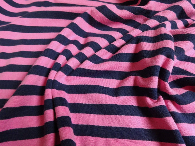 K&ouml;nnte beinhalten: Rosa-blauer gestreifter Stoff mit weicher, strukturierter Haptik. Der Stoff ist gefaltet und drapiert, wodurch die Textur und das Muster sichtbar werden.