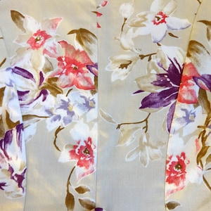 Puede incluir: Primer plano de una tela con un estampado floral. El dise&ntilde;o presenta grandes flores en tonos de rojo, morado, blanco y marr&oacute;n sobre un fondo beige claro. La tela parece ser un material ligero, posiblemente seda o un tejido delicado similar.