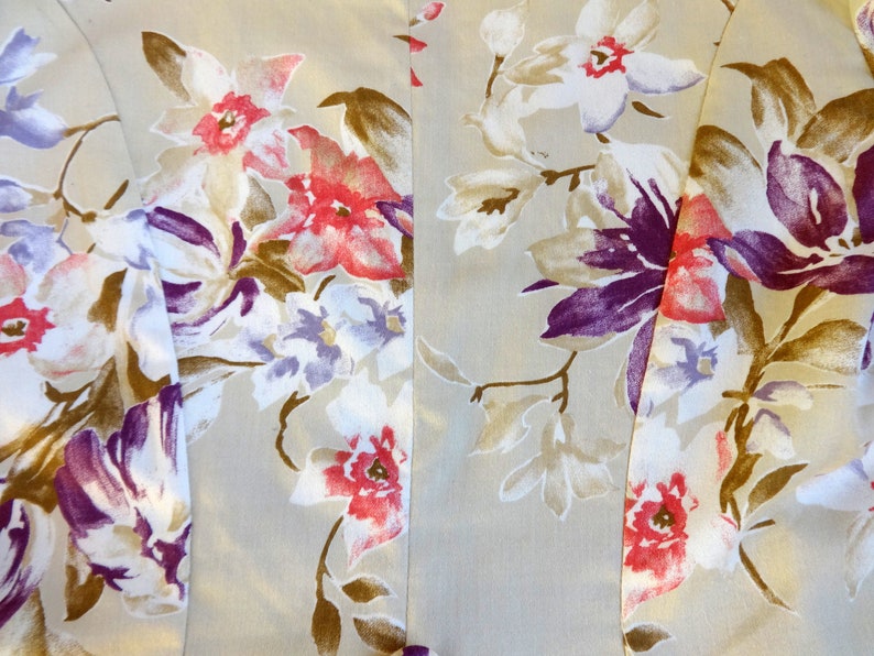Puede incluir: Primer plano de una tela con un estampado floral. El dise&ntilde;o presenta grandes flores en tonos de rojo, morado, blanco y marr&oacute;n sobre un fondo beige claro. La tela parece ser un material ligero, posiblemente seda o un tejido delicado similar.