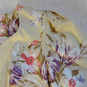 Puede incluir: Primer plano de una prenda color crema con estampado floral. El dise&ntilde;o presenta flores grandes en tonos morado, rosa y marr&oacute;n. La prenda tiene una etiqueta que dice "laura ashley".